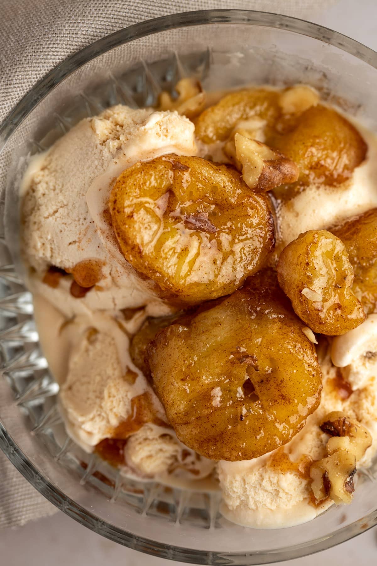 Up close view of caramelized bananas served in a glass bowl with walnut ice cream.