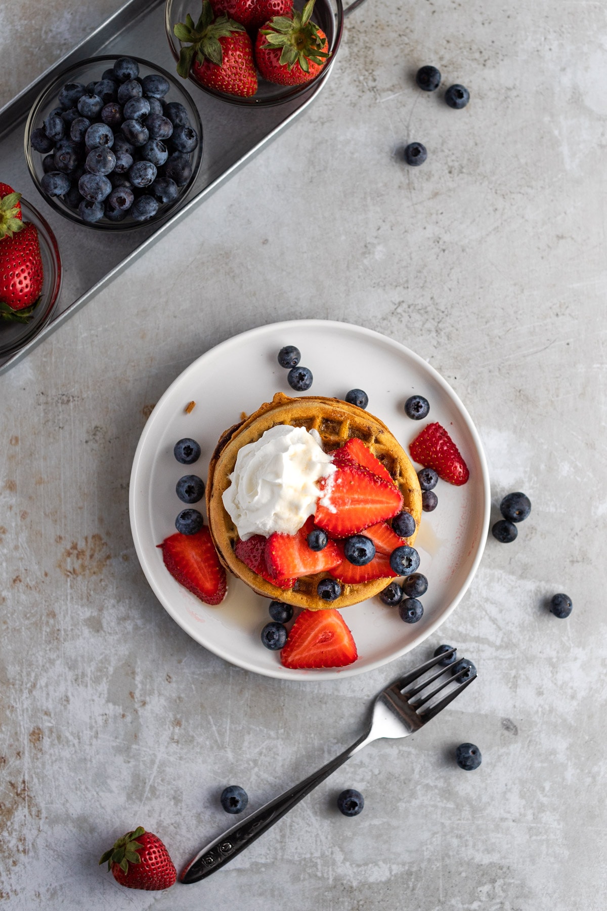 An overhead view of air fryer eggo waffles stacked on a round white plate, topped with strawberries and blueberries.