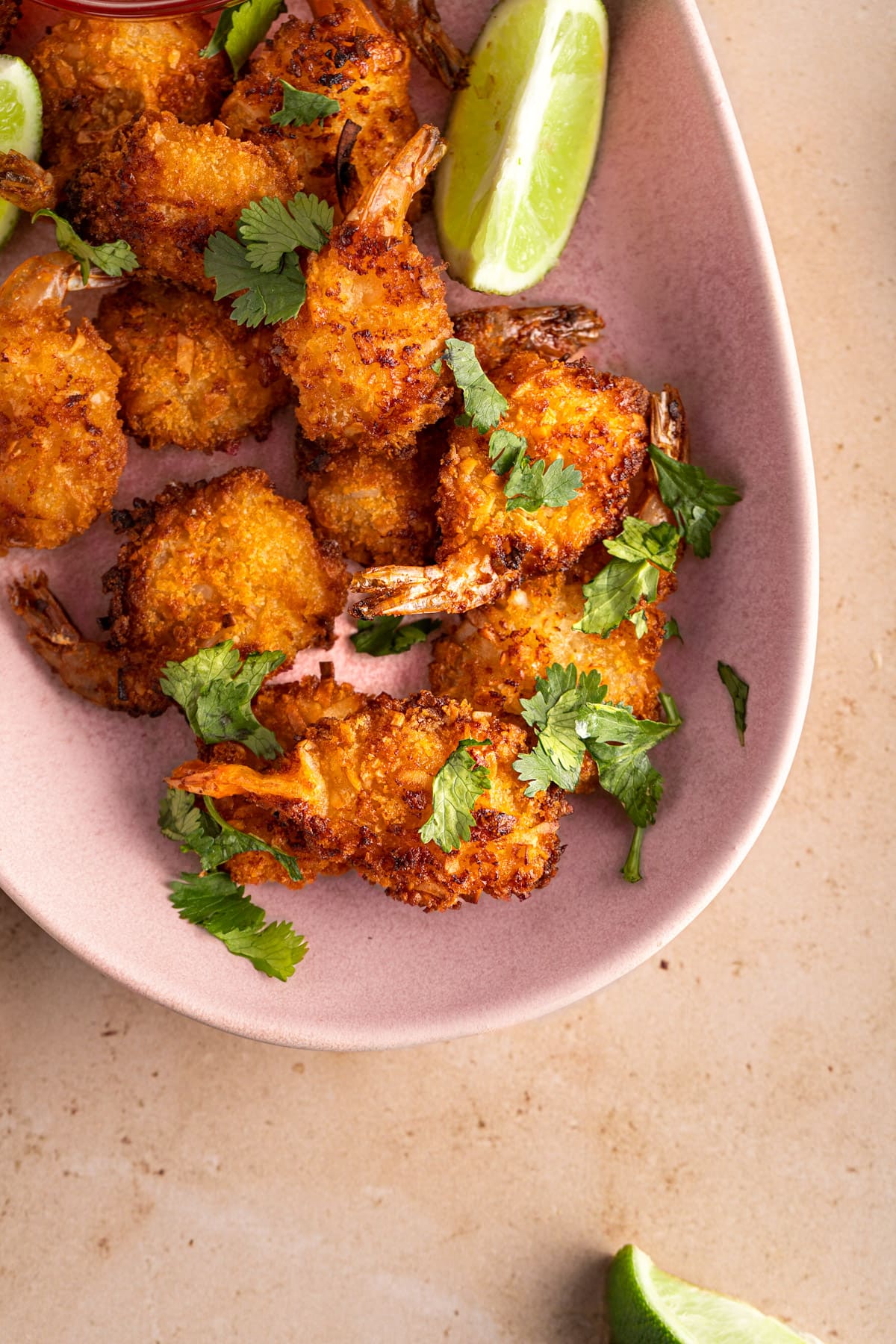 Overhead view of a pink oval serving platter full of cooked air fryer coconut shrimp, garnished with fresh cilantro.