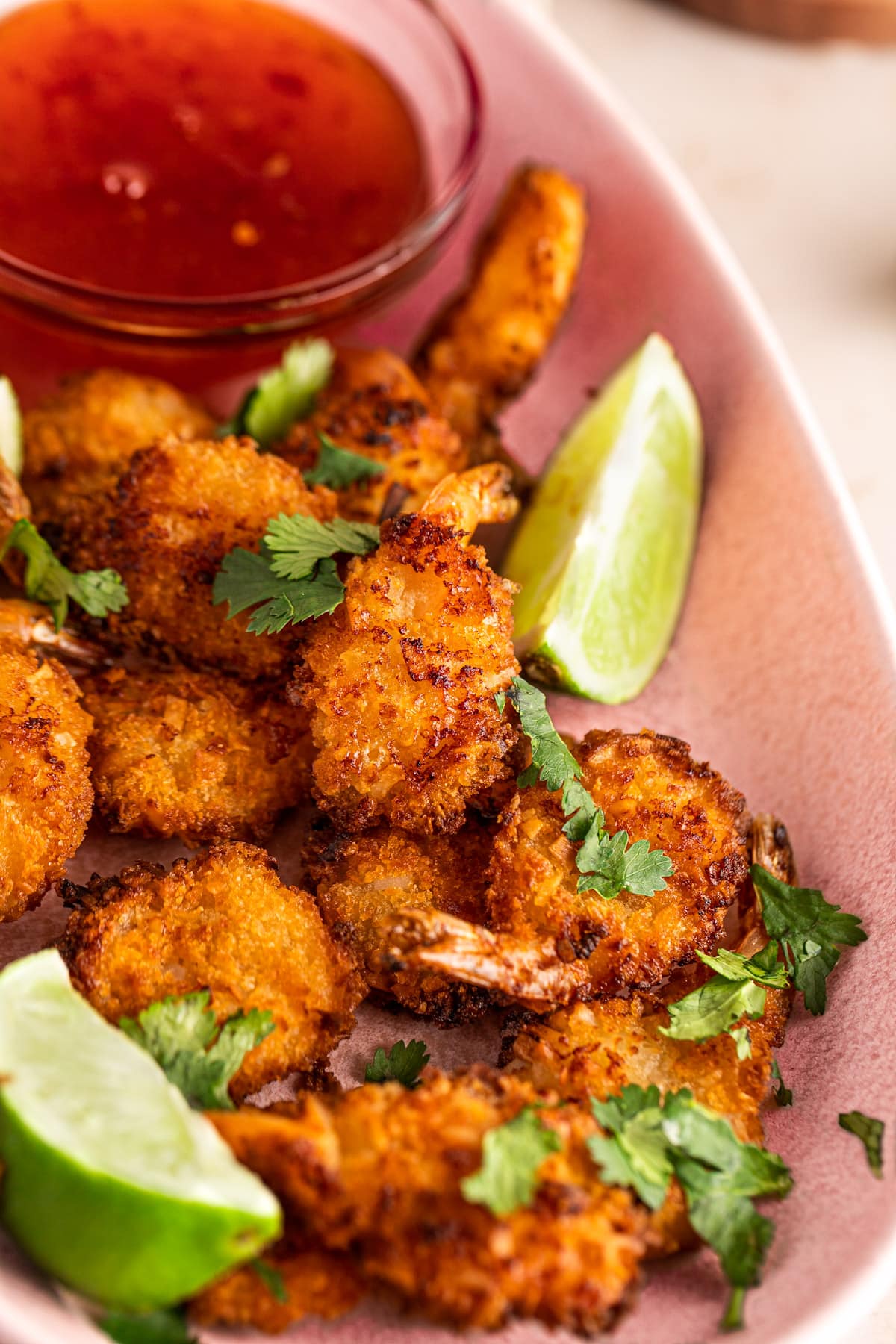 A plate of cooked air fryer coconut shrimp, garnished with lime slices and fresh cilantro.
