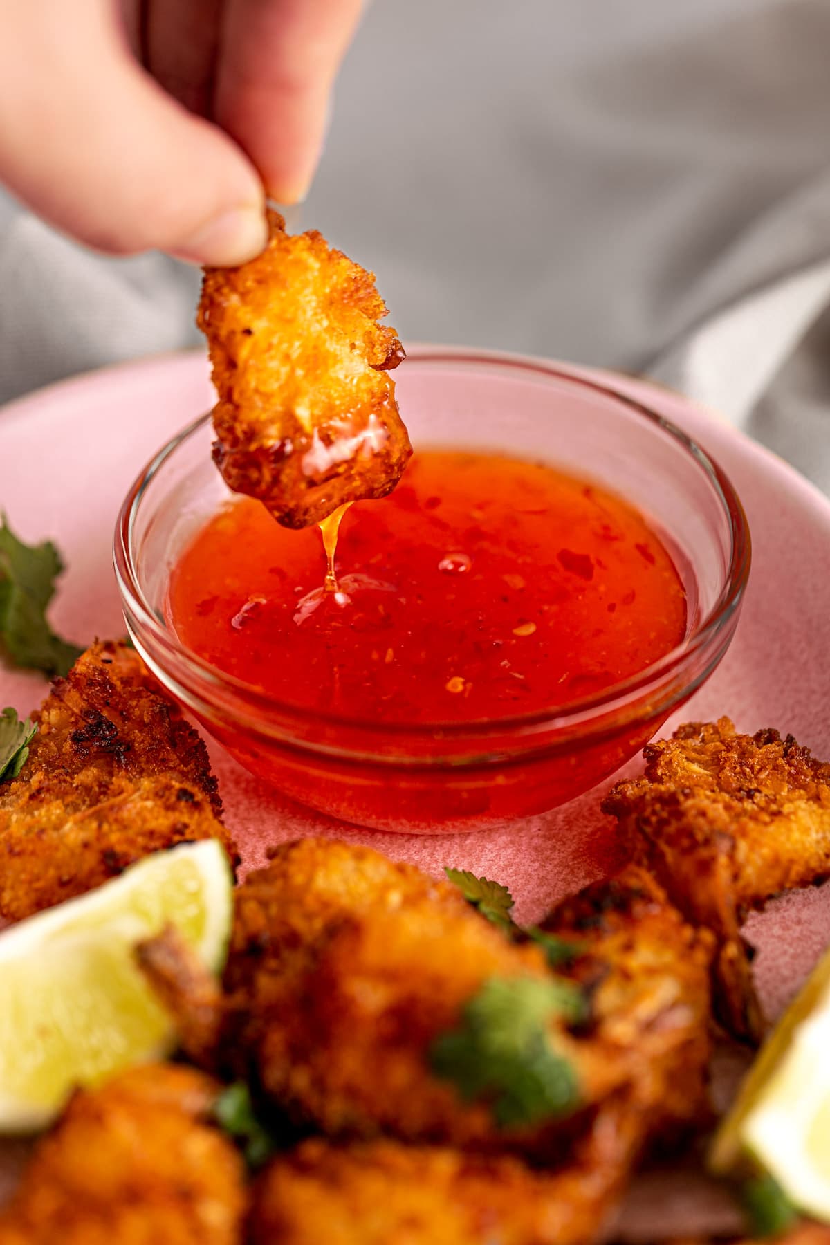 An air fryer coconut shrimp being dipped into red sweet chili dipping sauce.