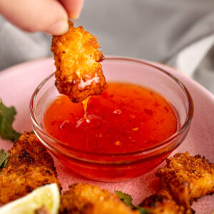 An air fryer coconut shrimp being dipped into red sweet chili dipping sauce.