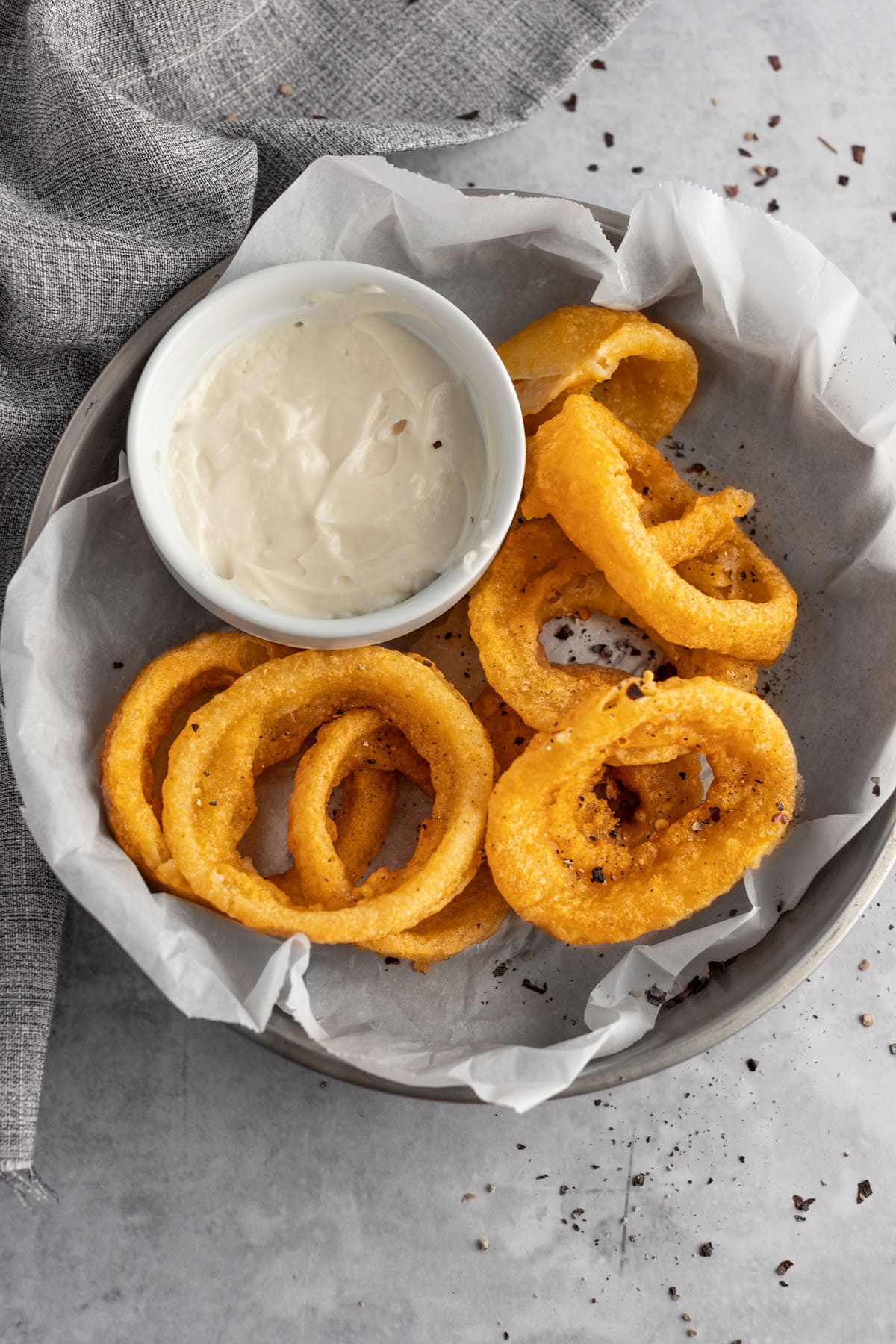 Air fryer frozen onion rings in a round metal tin lined with parchment paper next to a ramekin of mayo dipping sauce.