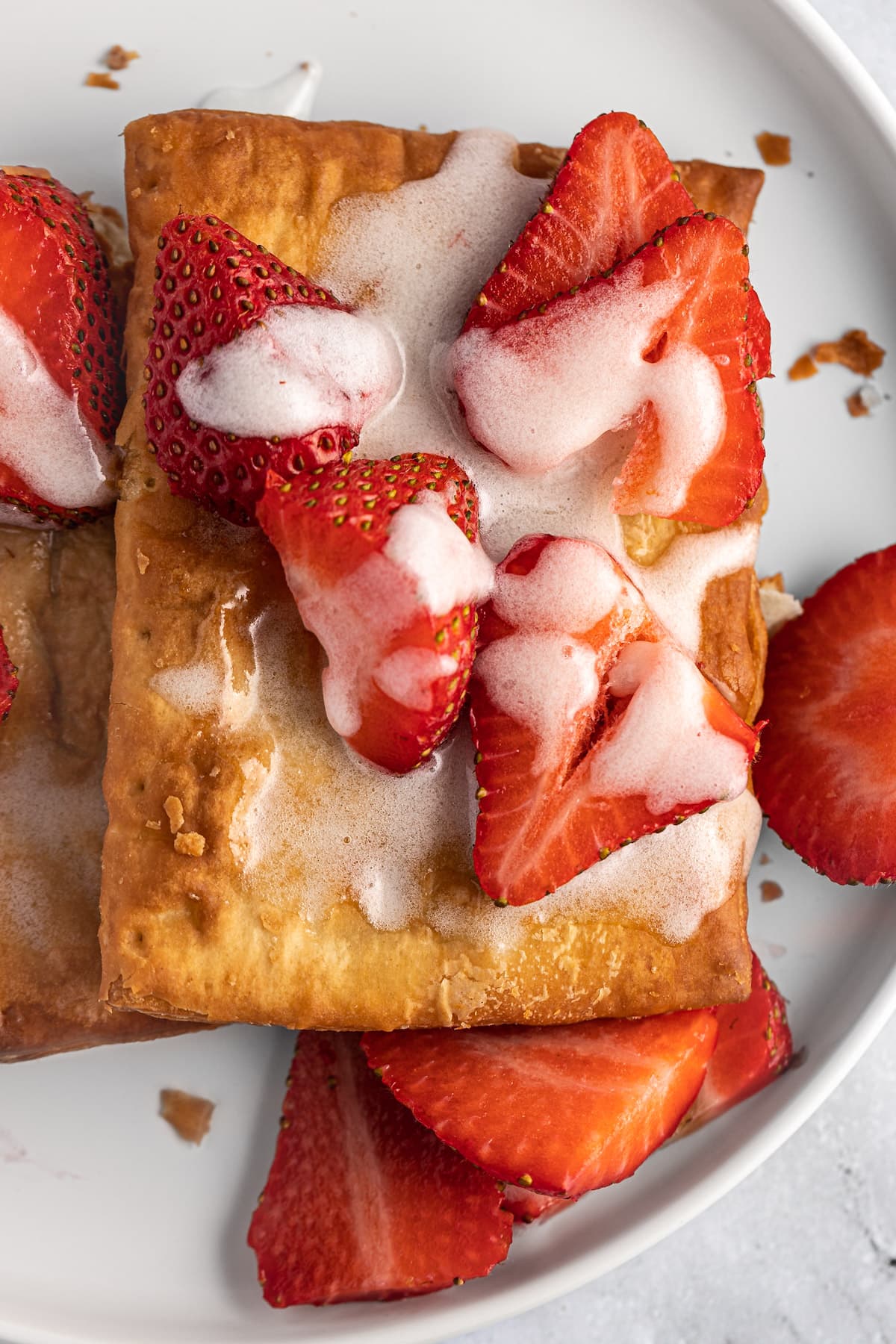 Up close overhead view on a frozen air fryer toaster strudel fresh out of the air fryer, topped with icing and fresh strawberries.