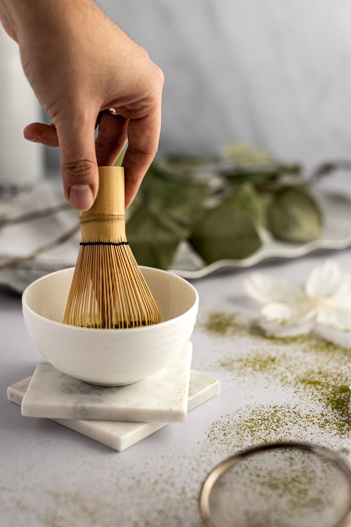 A holding a bamboo matcha whisk and stirring the matcha powder into the water to dissolve it.