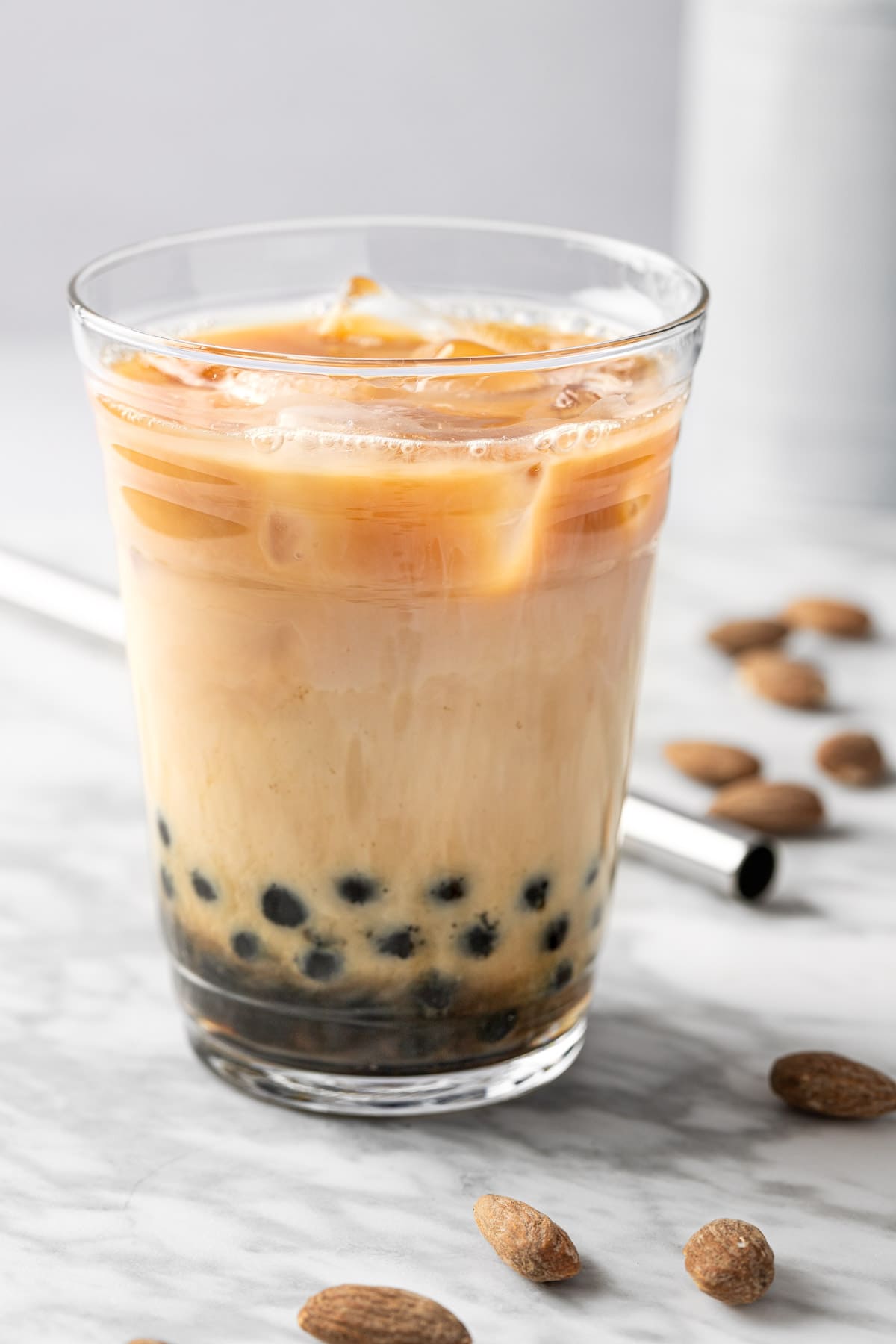 A glass of almond bubble tea with boba, on a white marble table.