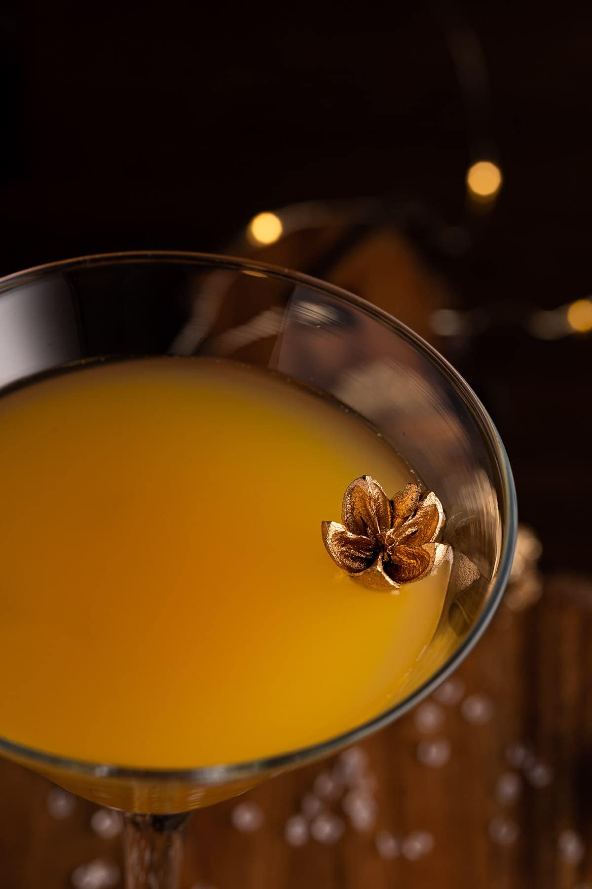 Up close view of the martini, garnished with a gold flower, on a dark, wooden background.