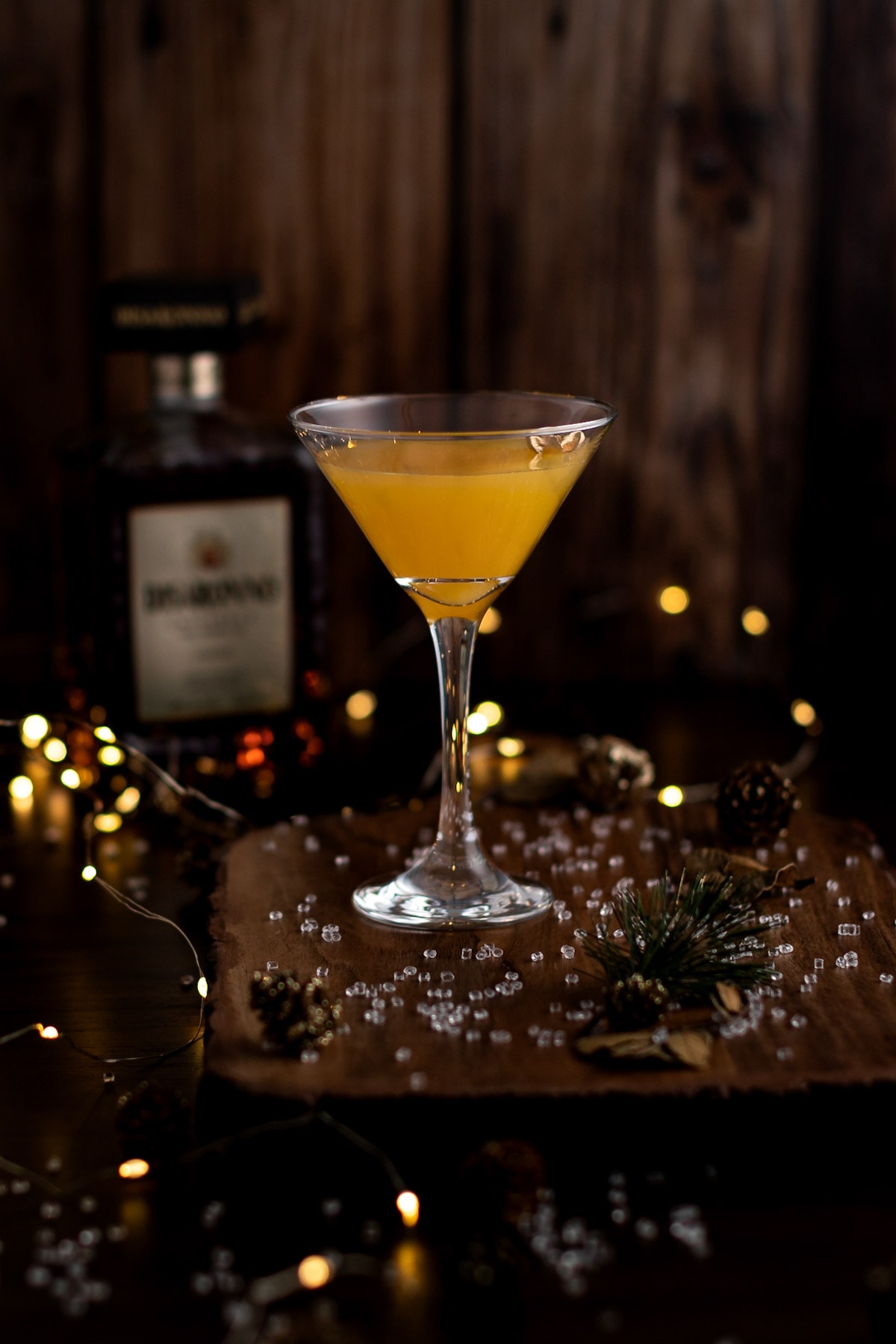 Peach amaretto martini on a wooden board, with fairy lights and a bottle of disaronno in the background.