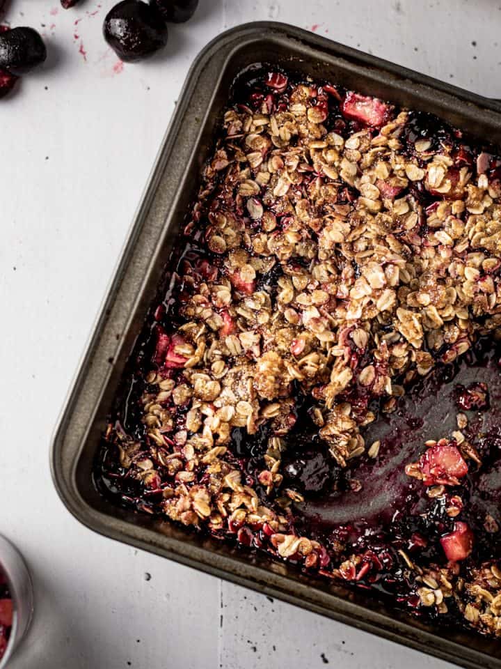Overhead view of baking dish with apple and cherry crumble, with some scooped out