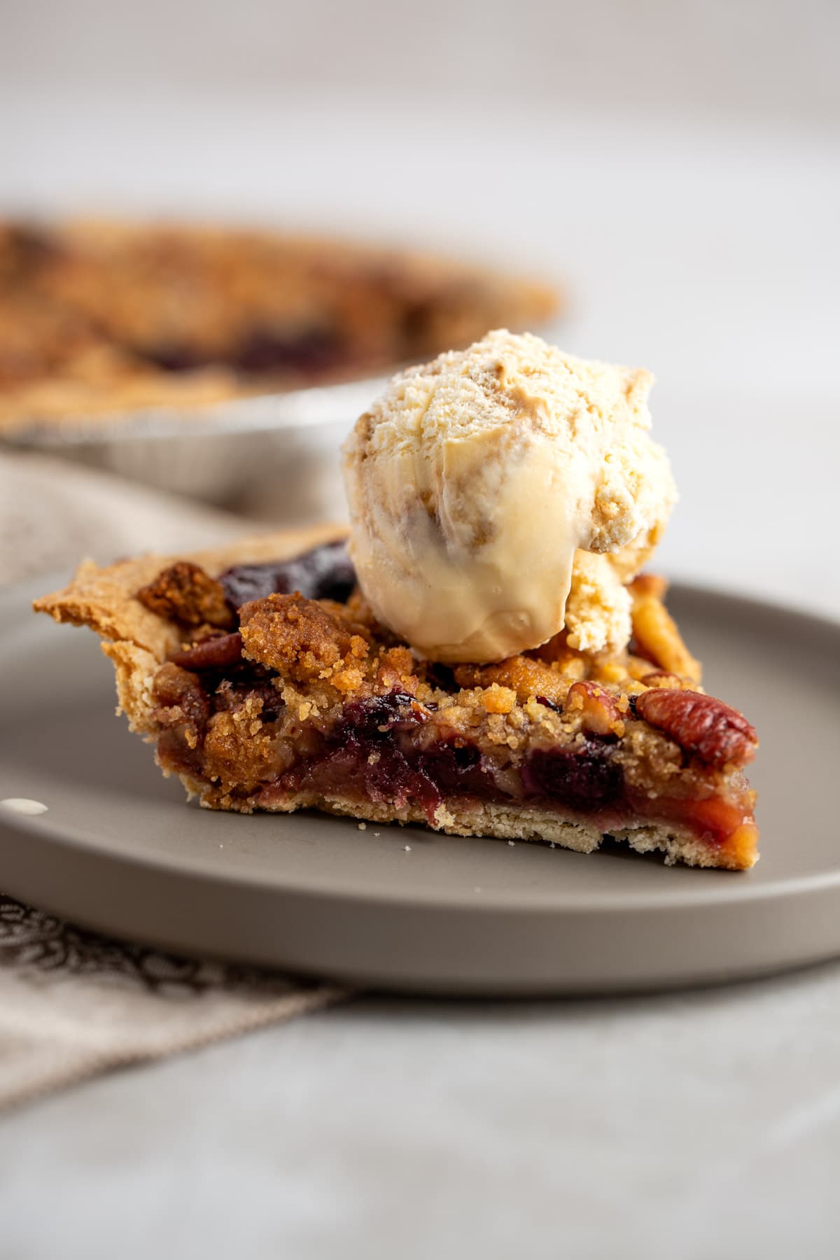 A slice of apple blueberry pie on a round brown plate, topped with a scoop of ice cream.