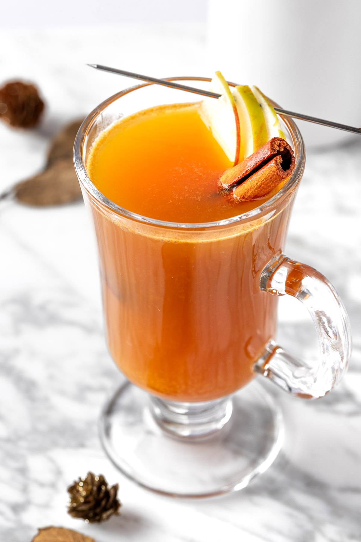 An apple cider hot toddy garnished with a cinnamon stick and apple slices.