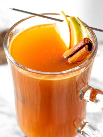 An apple cider hot toddy garnished with a cinnamon stick and apple slices.