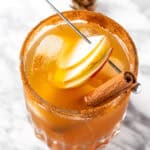 An apple cider margarita garnished with apple slices and a cinnamon stick.