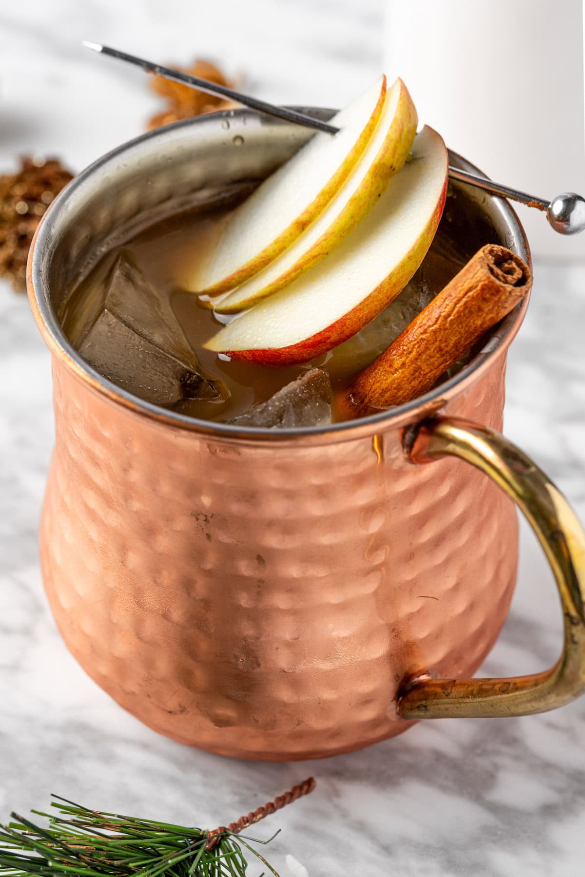 A fall moscow mule served in a copped mug and garnished with apple slices.