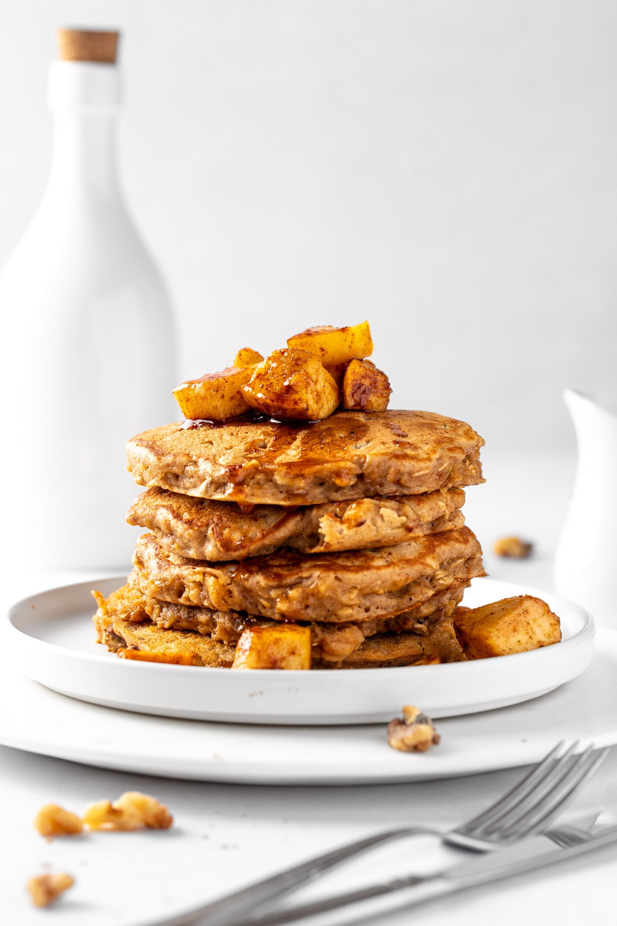 A stack of spiced apple pancakes on a round white plate, topped with cinnamon apples.