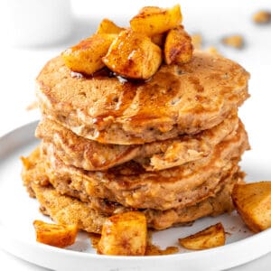 A stack of apple oat pancakes topped with spiced apples, sitting on a round white plate.
