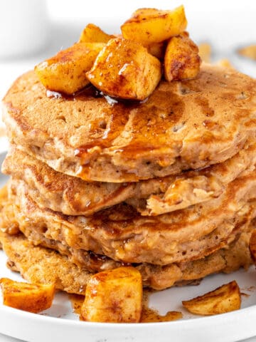 A stack of apple oat pancakes topped with spiced apples, sitting on a round white plate.