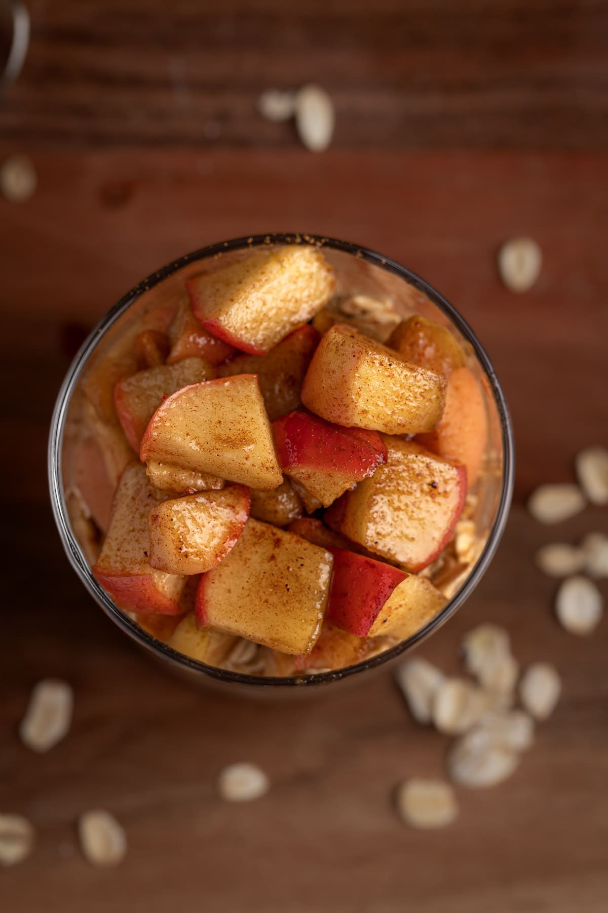 Overhead view of apple pie overnight oats on a wooden table with oats scattered around.