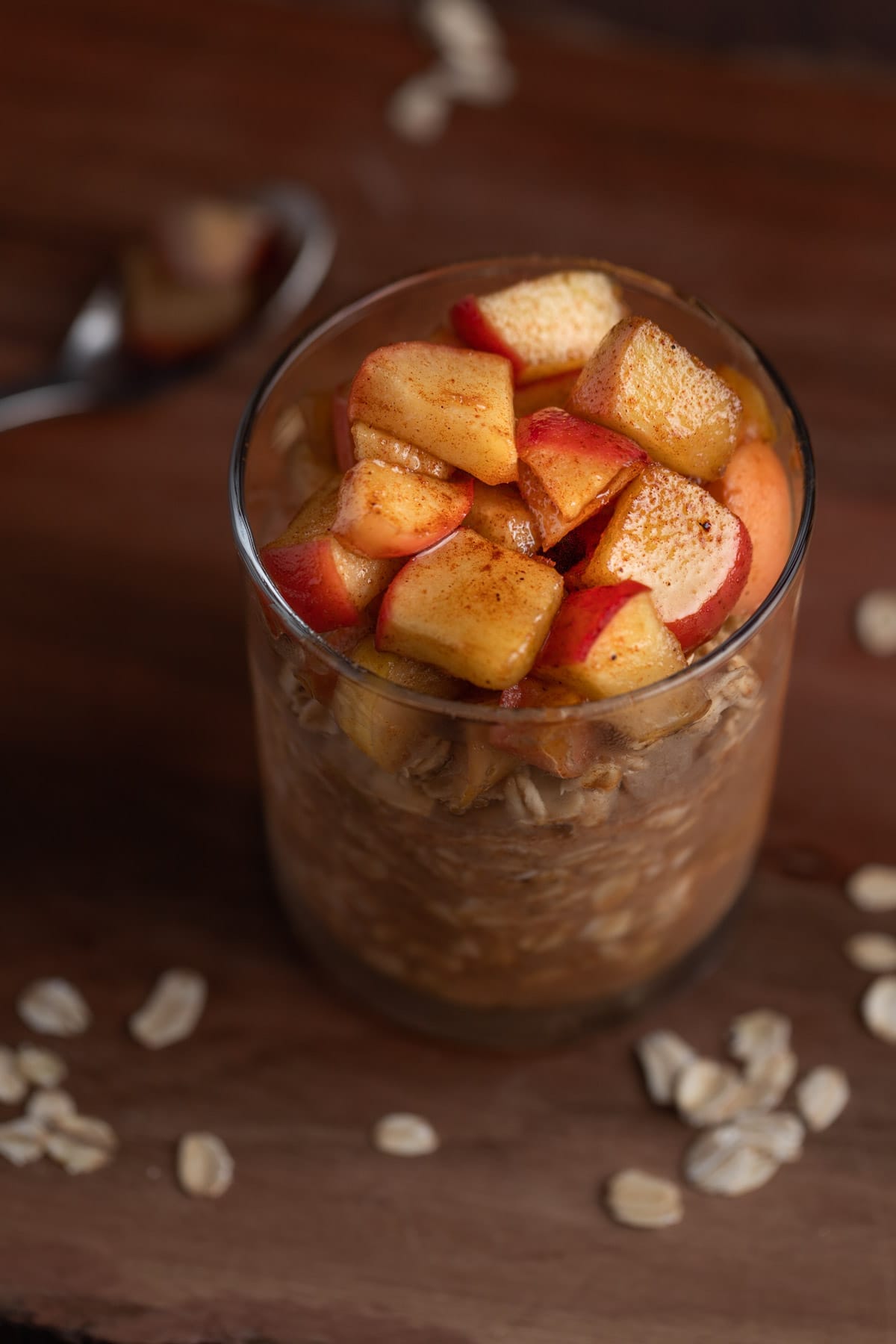 Apple pie overnight oats in a jar on a wooden table, topped with syrup covered apple chunks.