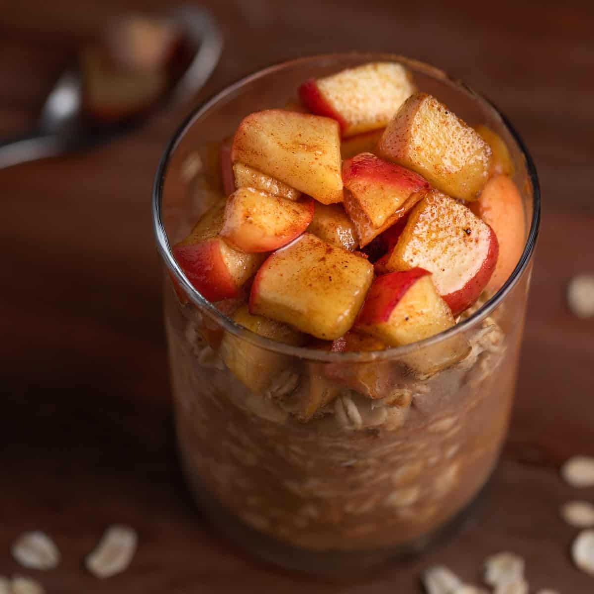 Apple pie overnight oats in a jar on a wooden table, topped with syrup covered apple chunks.
