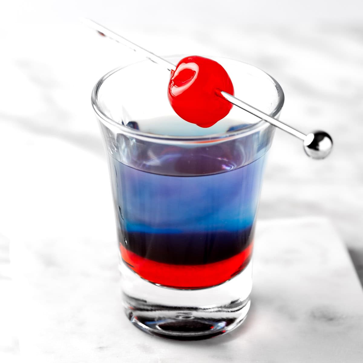 A layered Astro Pop Shot garnished with a maraschino cherry.