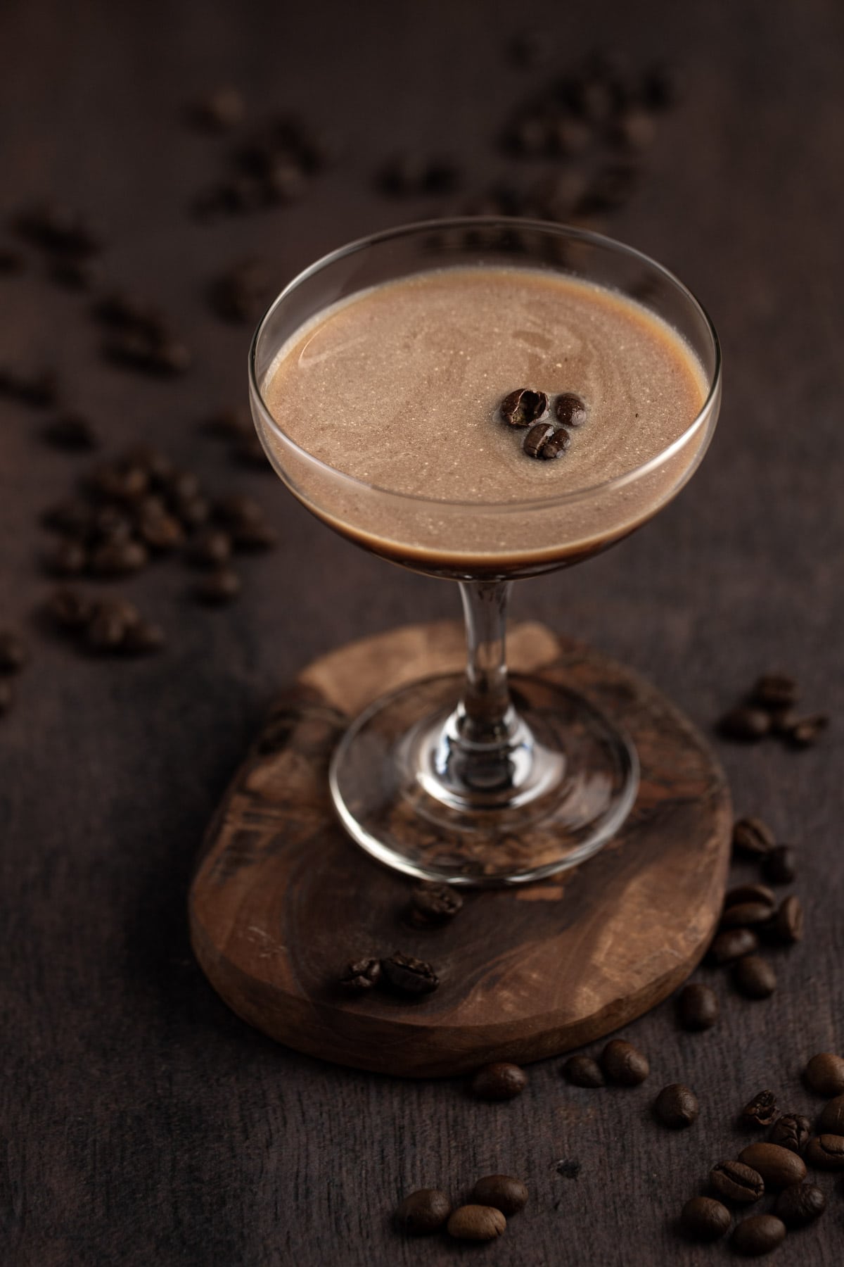 A baileys espresso martini in a coupe glass, garnished with coffee beans, on a wooden table.