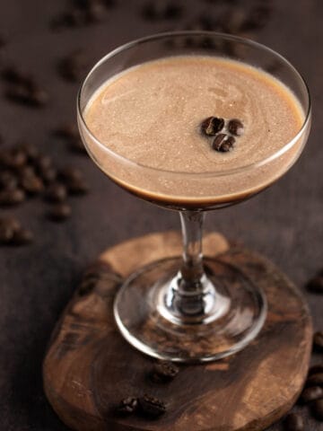 A baileys espresso martini in a coupe glass, garnished with coffee beans, on a wooden table.
