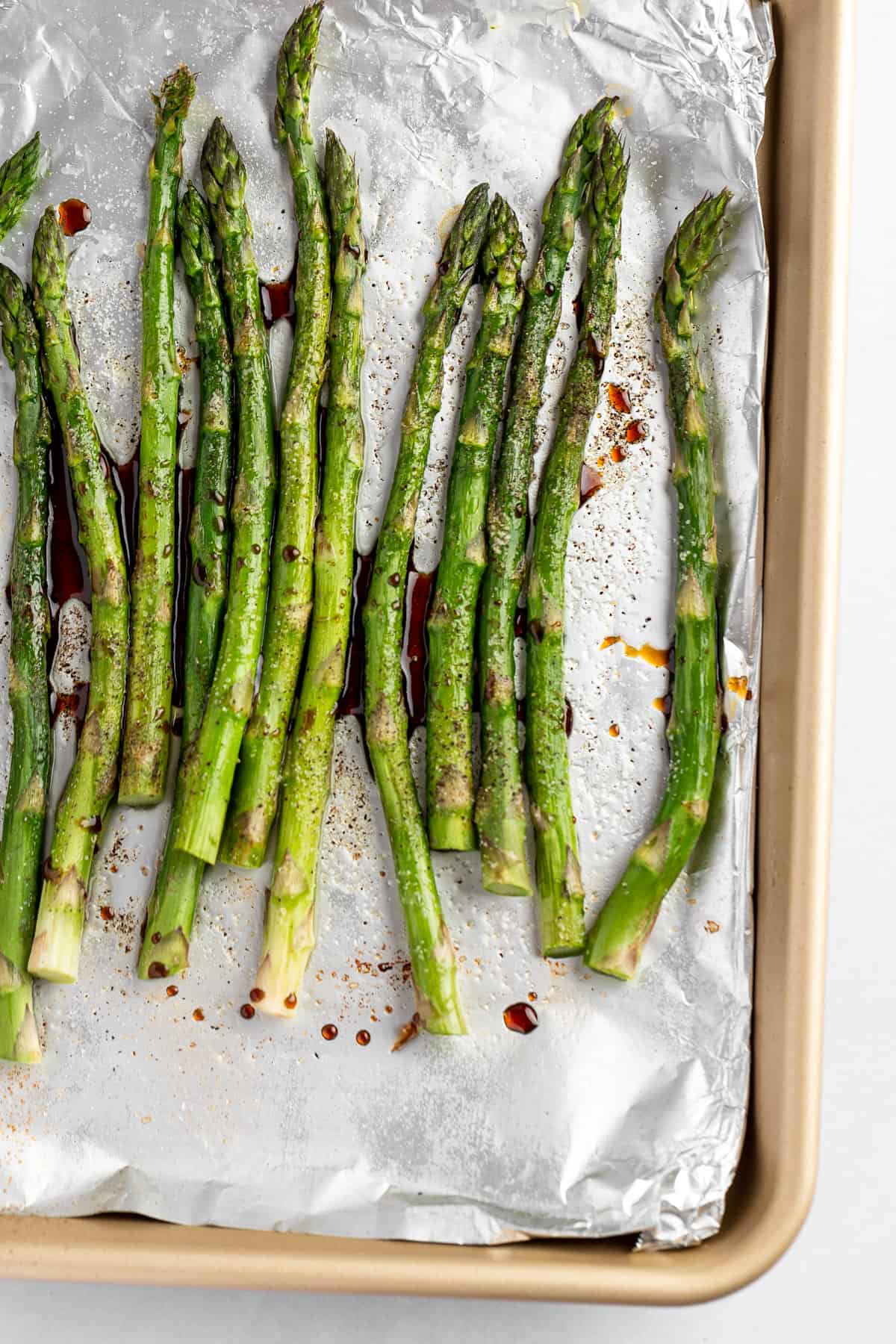 Roasted asparagus with balsamic glaze, on a gold baking tray covered in aluminum foil.