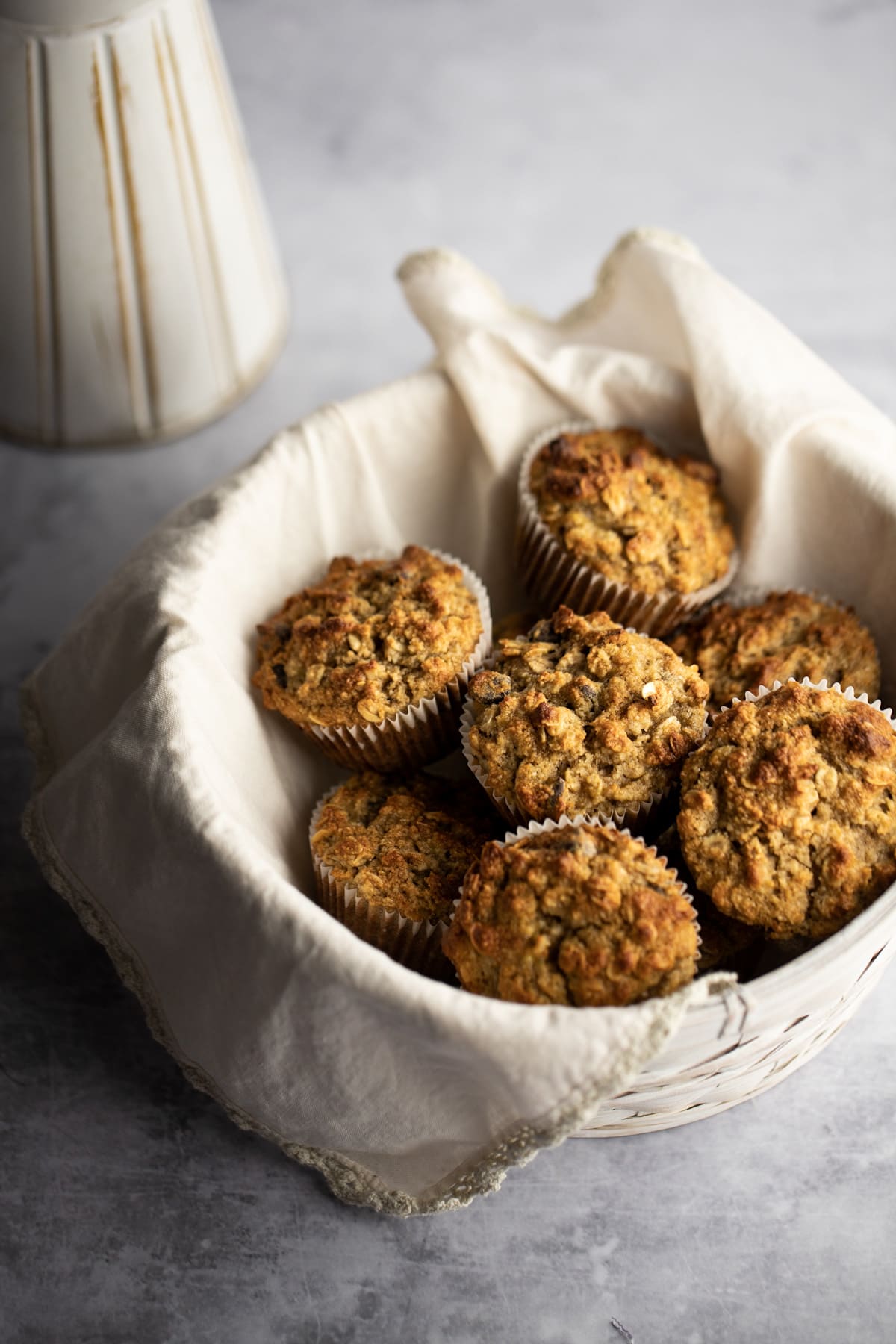 A white basket with a beige napkin filled with muffins, on a grey table.