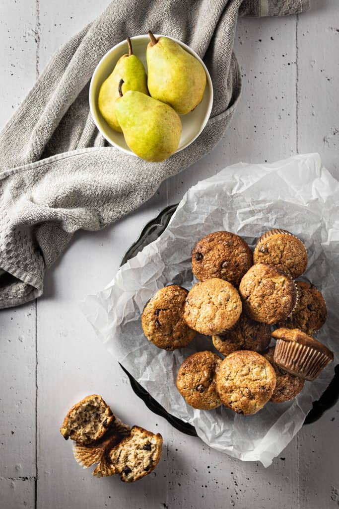 Overhead view of a bowl of muffins, a bowl of pears and a cut open muffin