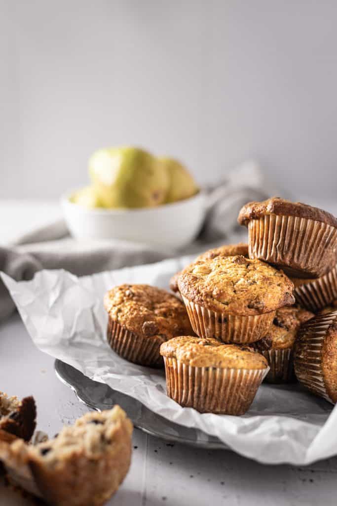 A side angle view of a plate of pear banana muffins with pears in the background