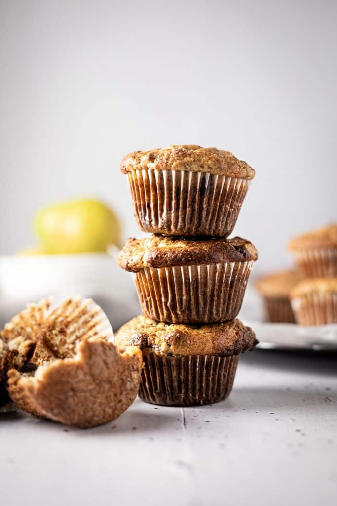Three banana and pear muffins stacked on top of each other, with a half eaten one lying in front