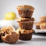 Three banana and pear muffins stacked on top of each other, with a half eaten one lying in front