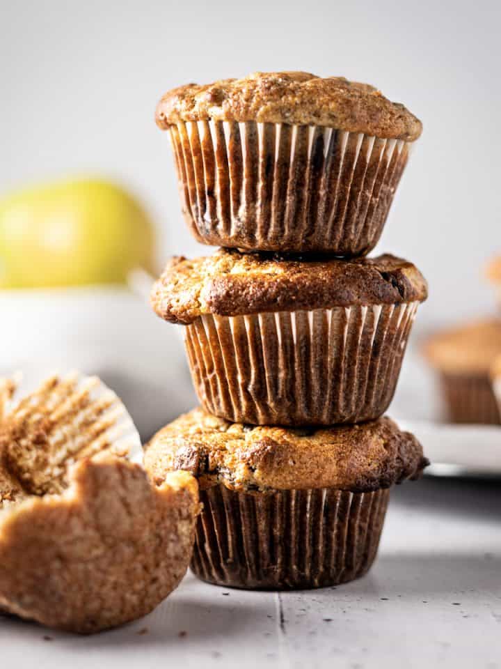 Three banana and pear muffins stacked on top of each other, with a half eaten one lying in front