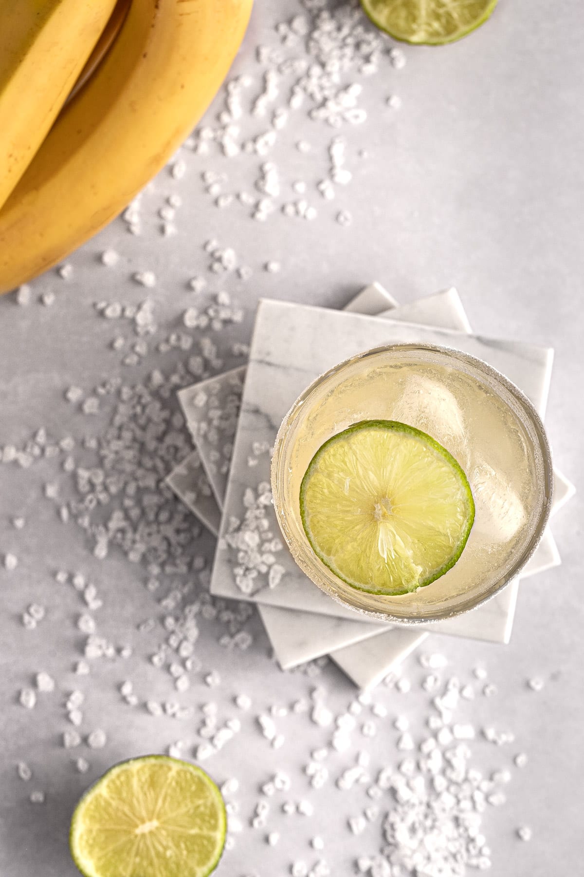 Overhead view of a banana margarita with a slice of lime in the glass, on a white table.