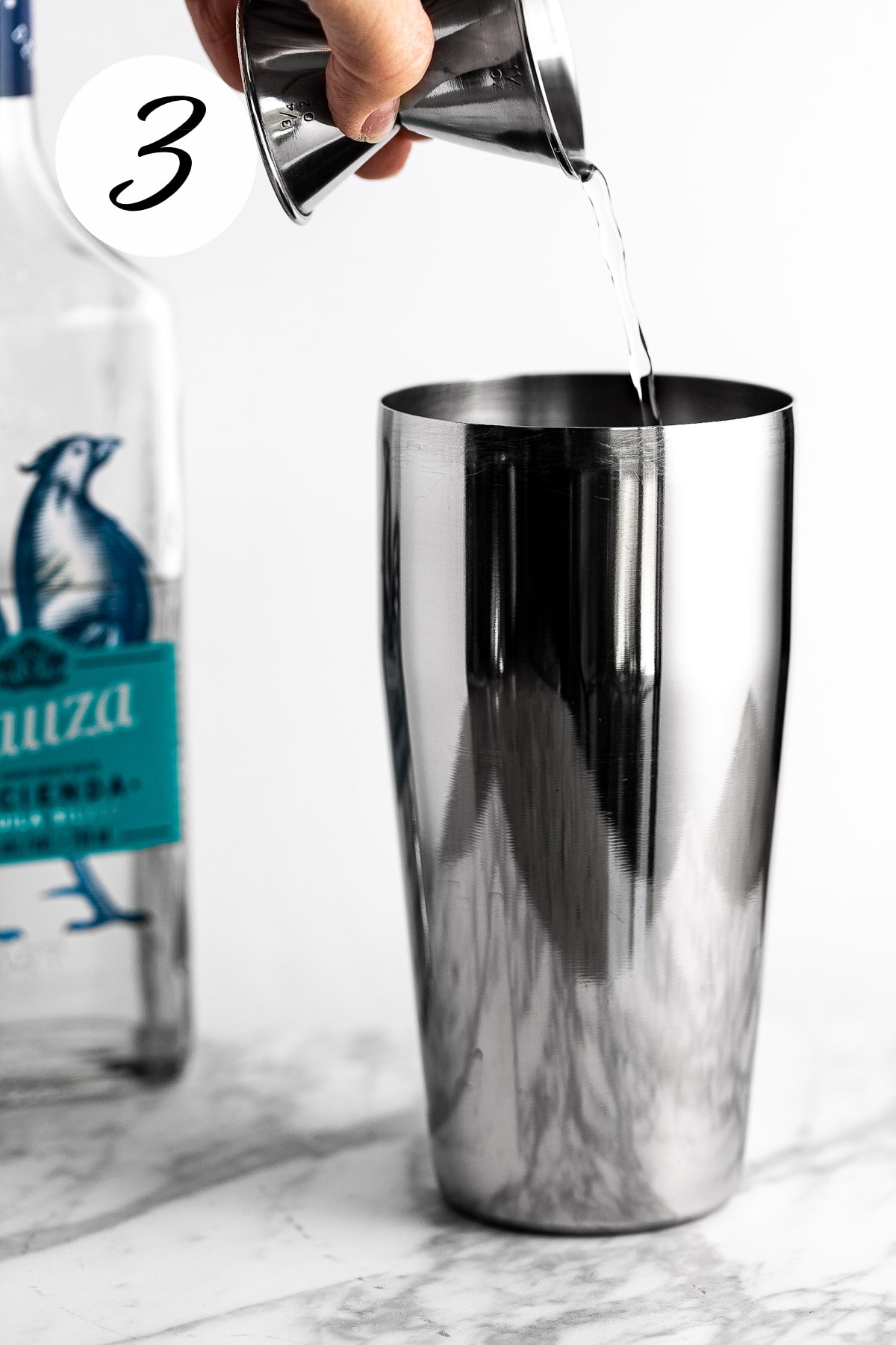 A process photo illustrating step 3: Tequila being poured into a cocktail shaker.