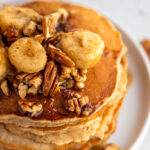 Up close view of bananas foster pancakes topped with walnuts, pecans and banana slices.
