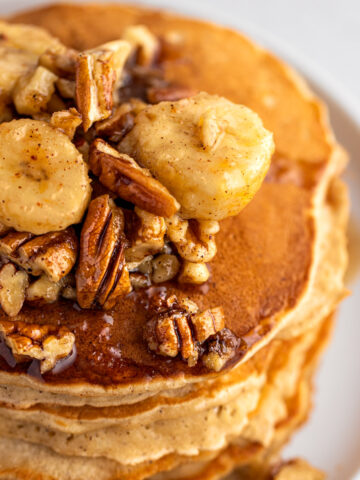 Up close view of bananas foster pancakes topped with walnuts, pecans and banana slices.