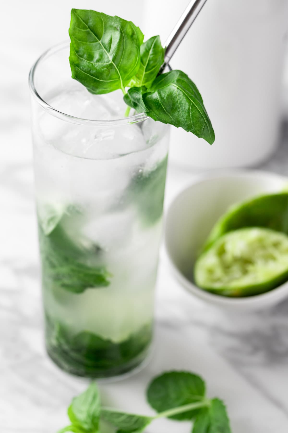 A basil mojito garnished with mint and basil leaves, sitting on a white marble table.