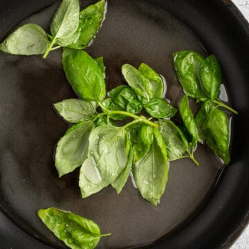 Fresh basil leaves cooking in a stovetop pan to make basil simple syrup.