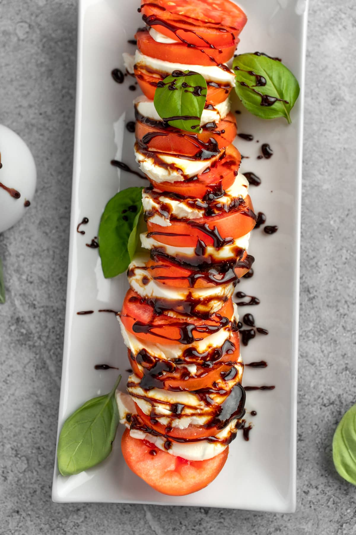 Caprese salad on a white rectangular plate, garnished with fresh basil leaves and drizzled with balsamic glaze.