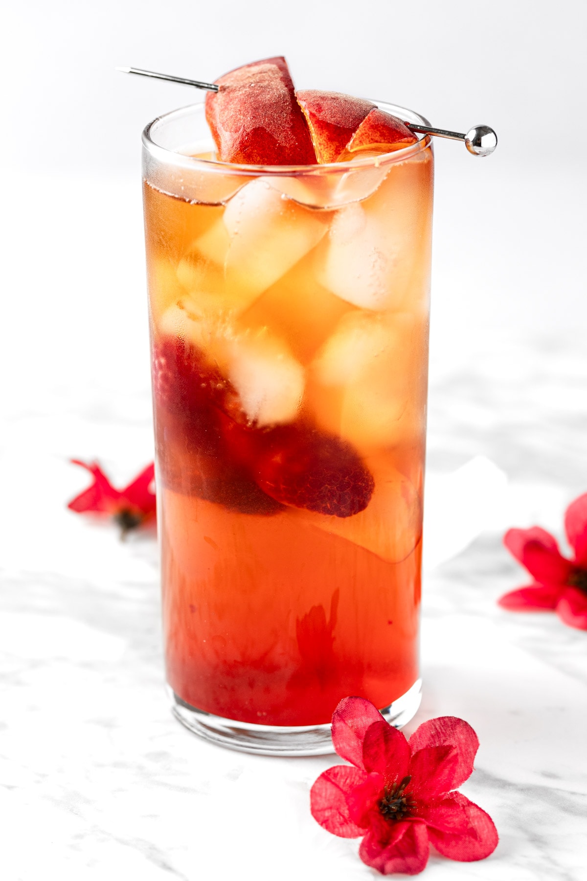 A bellini peach raspberry iced tea next to red flowers on a white marble table.