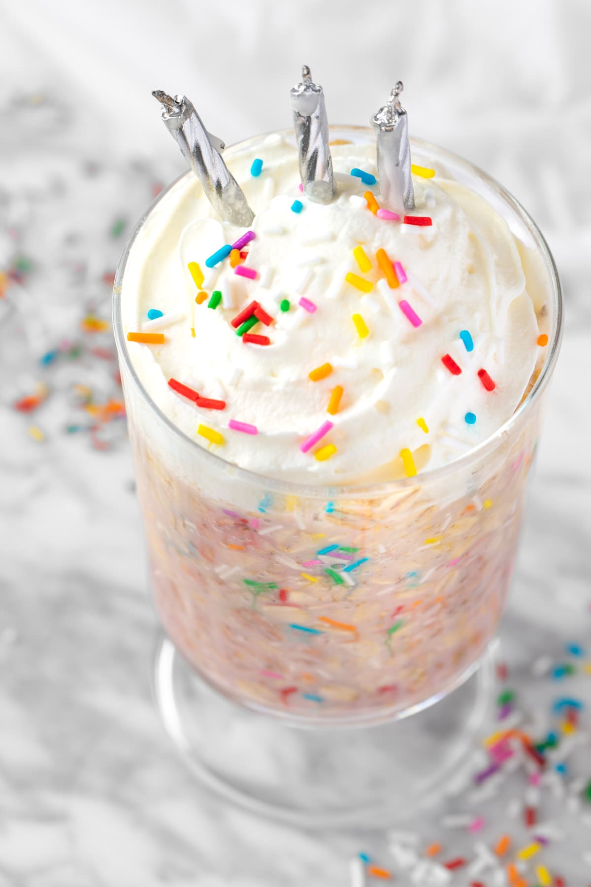 Cake batter oats with multicolored sprinkles, topped with whipped cream and silver candles.