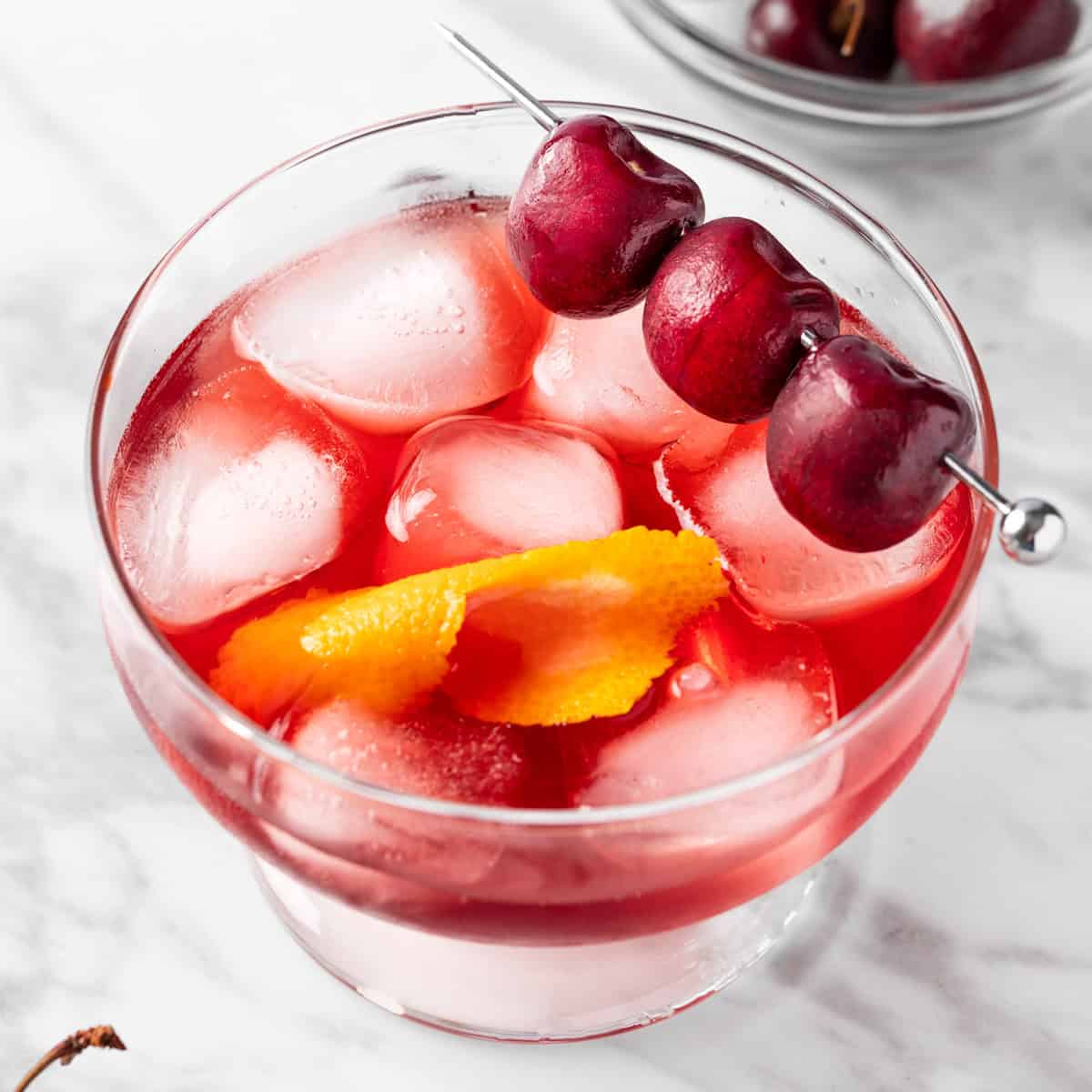 A Black Cherry Old Fashioned cocktail garnished with fresh cherries.