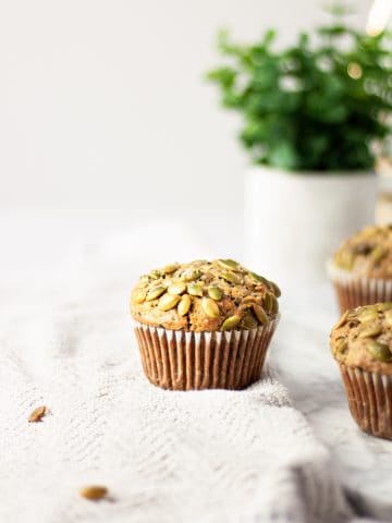 Three black sesame muffins on a light grey towel with a green plant in the background.