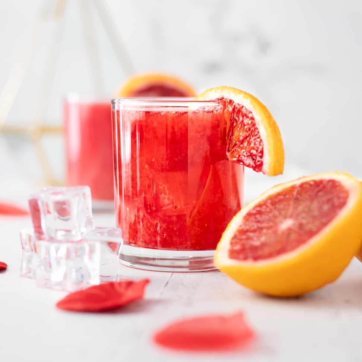 Blood orange whiskey sour cocktail, garnished with a slice of blood orange, on a white background. 