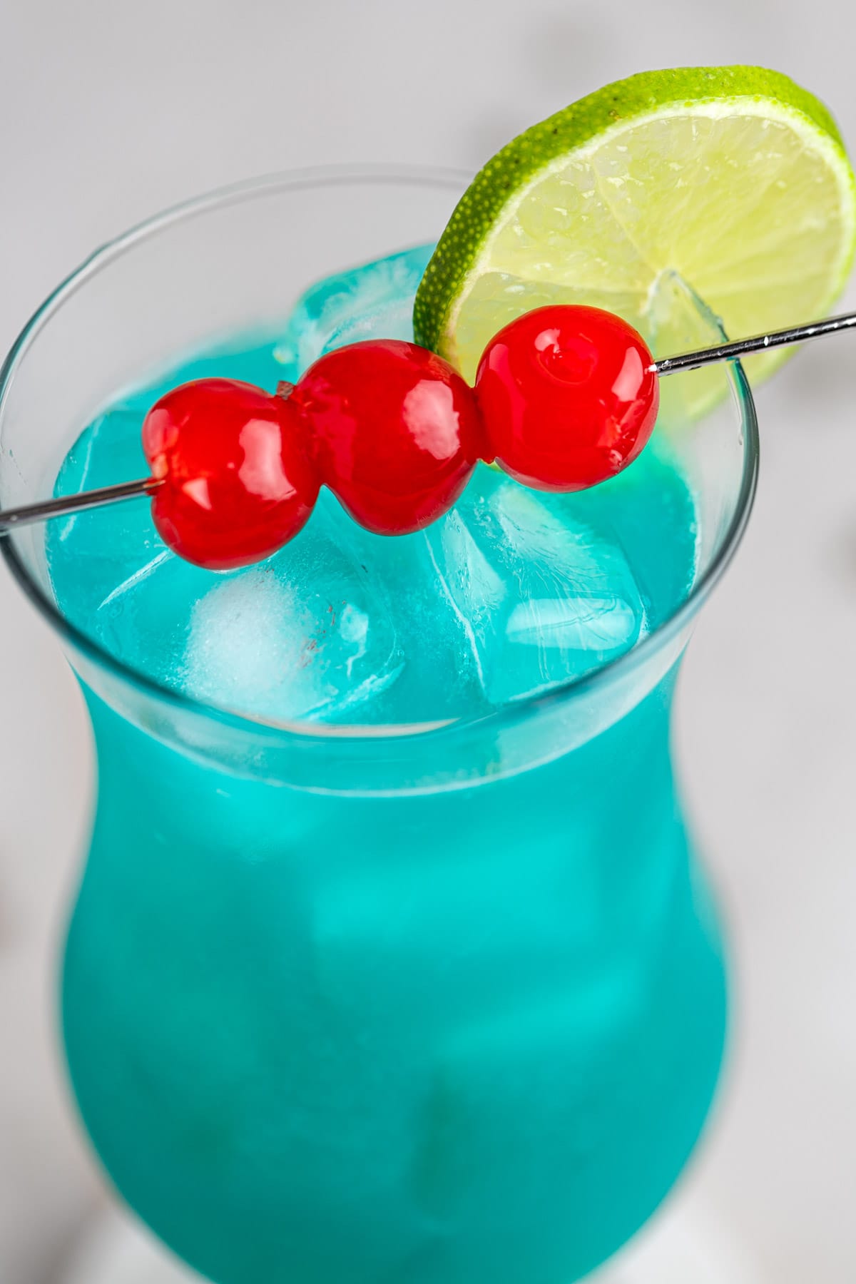 Up close view of a hurricane cocktail, garnished with cherries and a lime slice.