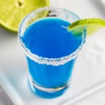 An overhead view of a blue kamikaze shot with a sugar rim, garnished with a slice of lime.