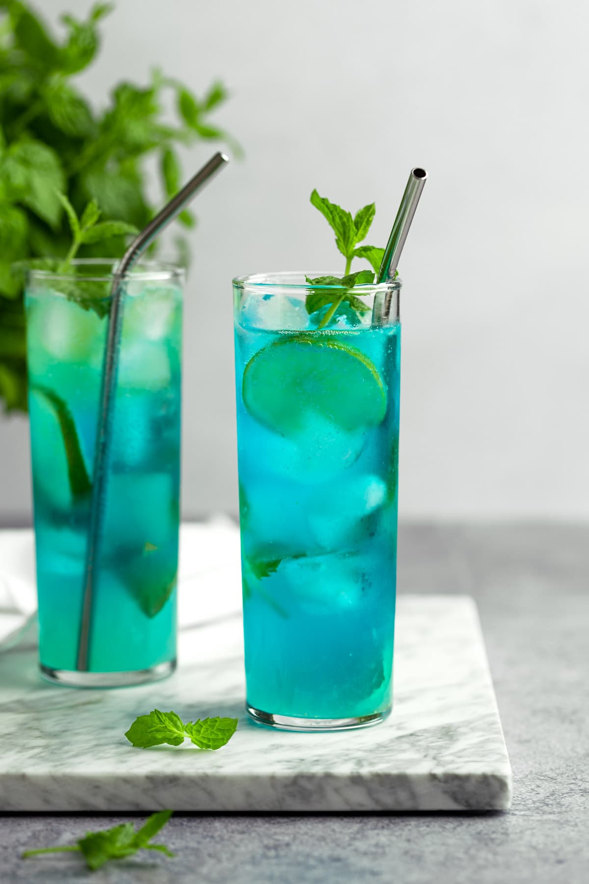A couple blue mojitos garnished with lime slices and mint leaves.