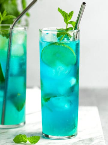 A couple blue mojitos garnished with lime slices and mint leaves.